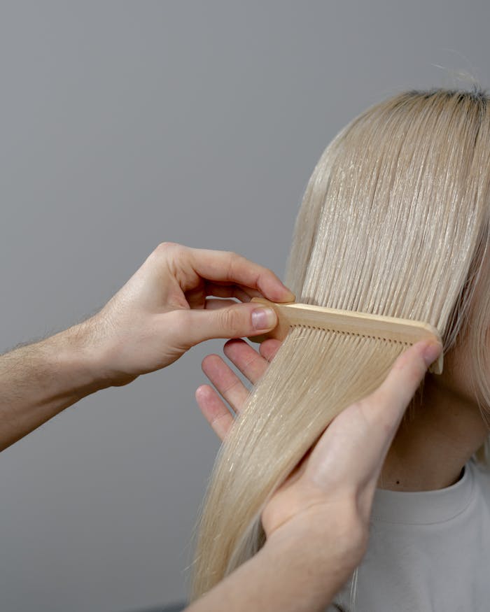 Close-up of a hairstylist combing blonde hair, showcasing attention to detail.