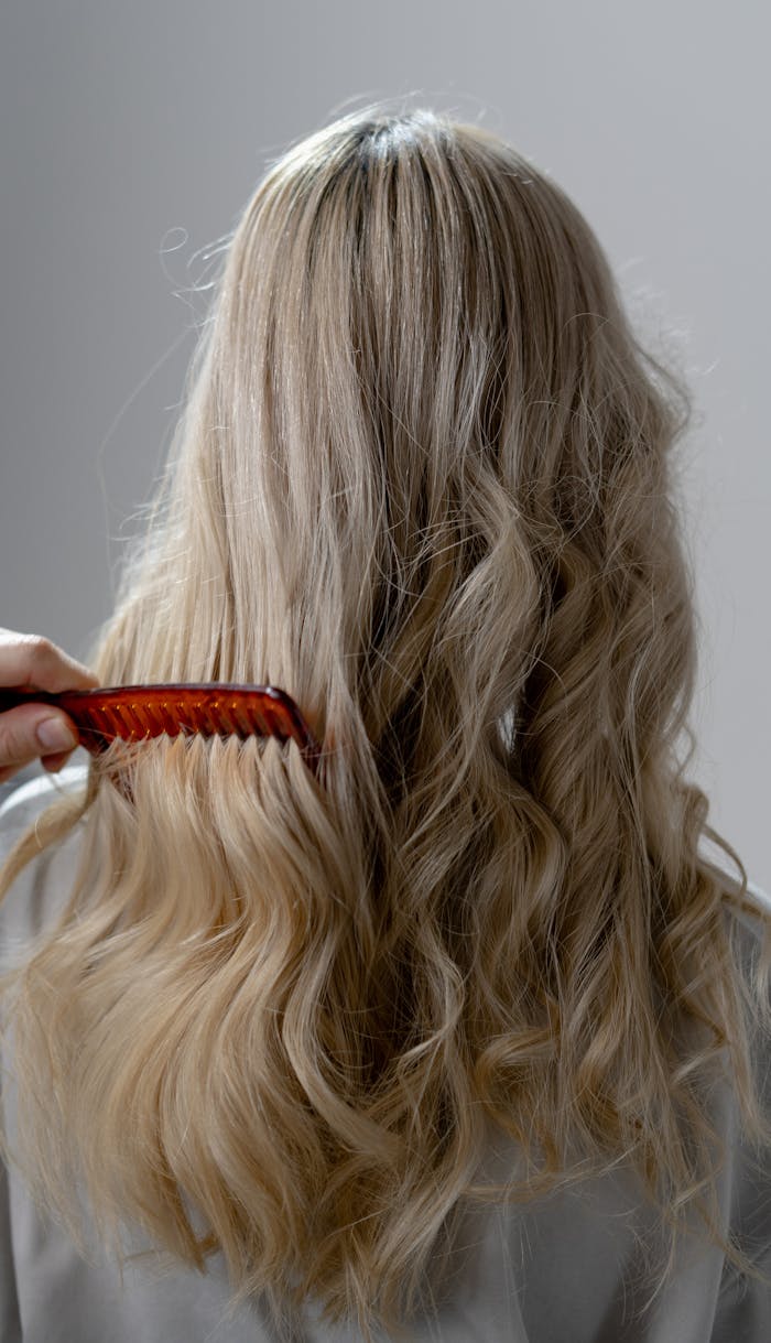 Back view of long blonde hair being combed into smooth curls with a red comb.
